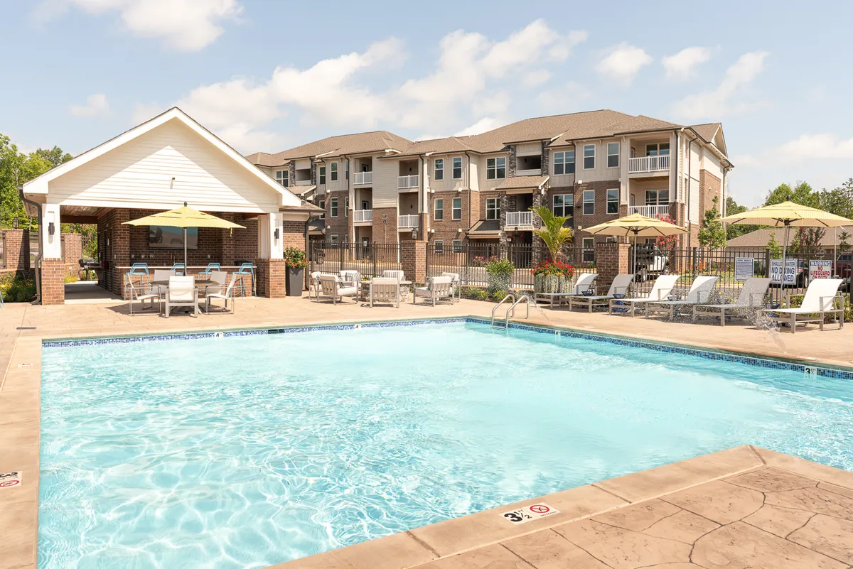 This image features a sparkling swimming pool surrounded by cabanas, lounge chairs, umbrella seating, and well-maintained landscaping. People are seen swimming, sunbathing, and socializing, with a relaxed, leisurely mood. The setting is ideal for both quiet personal relaxation and lively community gatherings, reflecting a resort-like ambiance.