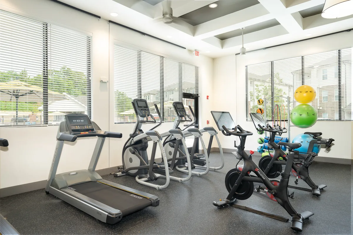 A bright, energetic fitness center with treadmills, elliptical machines, stationary bikes, and exercise balls. The space is modern and well-lit, conveying a sense of motivation and community as residents engage in workouts and group fitness activities.