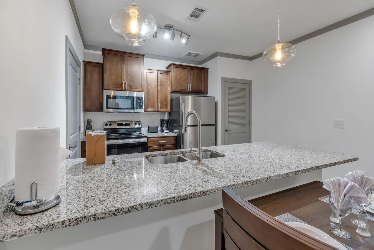 A beautifully appointed open kitchen and dining area with granite countertops, wood cabinets, stainless steel appliances, and a dining table set for a meal. The space feels welcoming and perfect for both meal prep and entertaining guests.