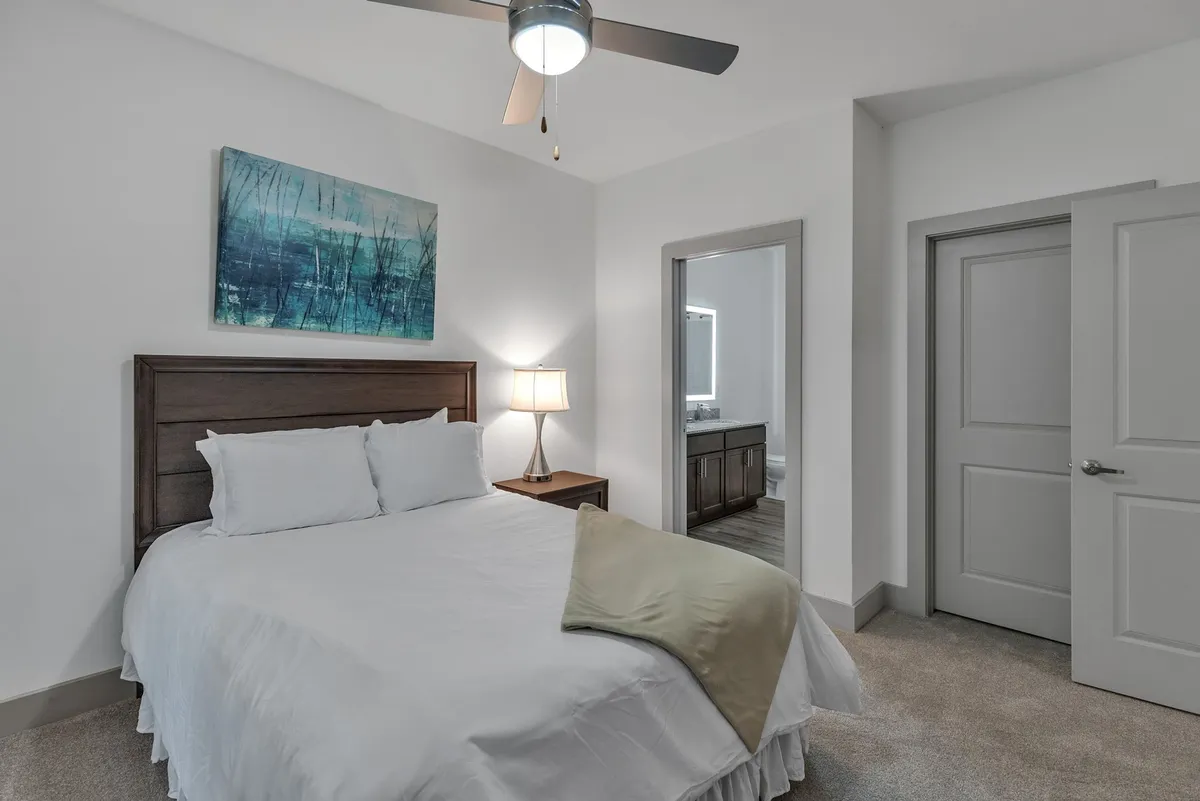 A cozy bedroom scene featuring a comfortable-looking bed with soft linens, a warm lamp on the bedside table, and tasteful wall art above the headboard. The overall atmosphere is calm and inviting, ideal for winding down after a busy day.