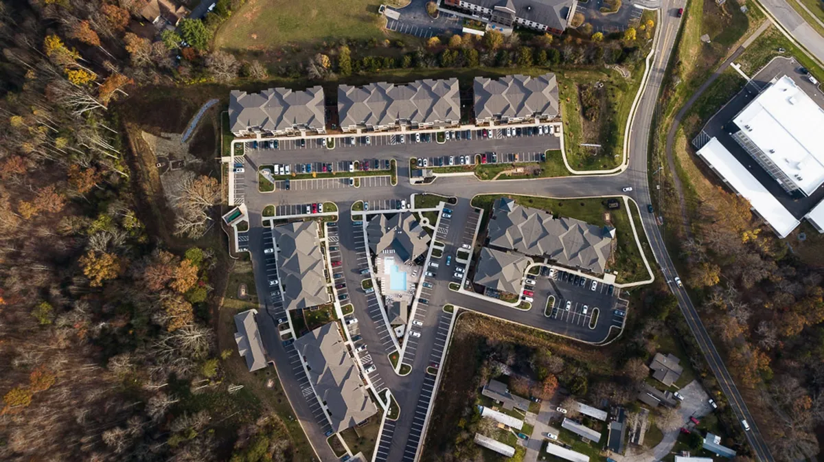 The image features The Overlook's resort-style swimming pool area surrounded by greenery, with visible building layouts and a parking area. The space is vibrant and lively, hinting at opportunities for relaxation, productivity, and community activities.