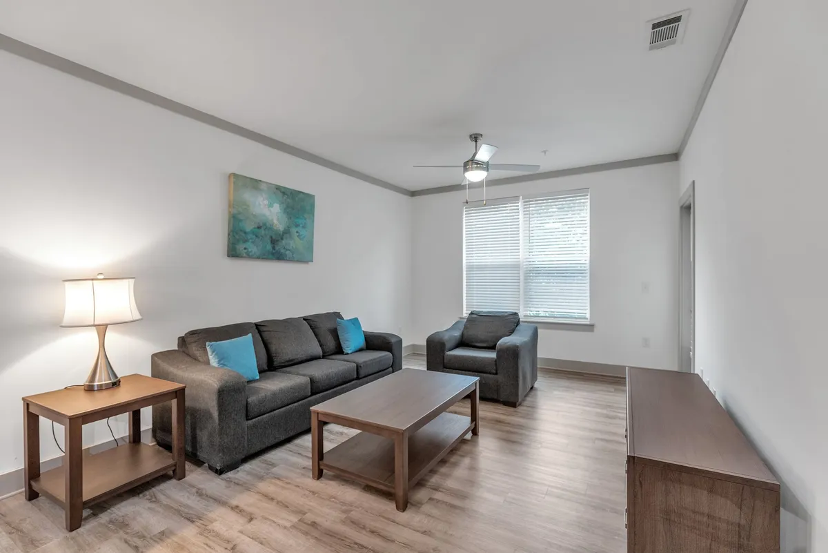 A cozy living room scene featuring a plush sofa, accent chair, coffee table, lamp, and eye-catching artwork. Warm lighting creates an inviting atmosphere perfect for relaxing, socializing, or watching TV.